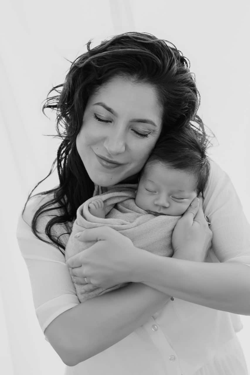 Maman tenant son bébé emmailloté contre elle pendant une séance naissance