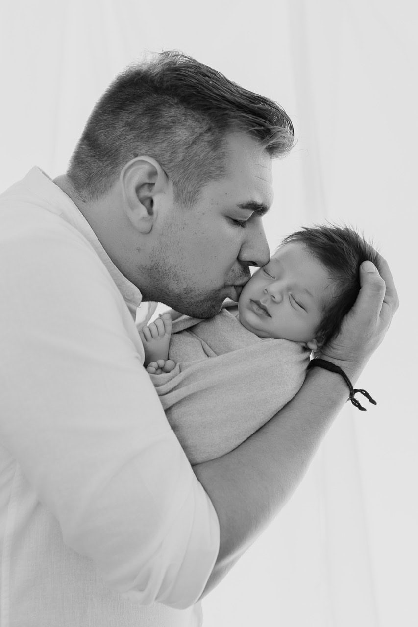 Papa embrassant son nouveau-né emmailloté pendant une séance naissance