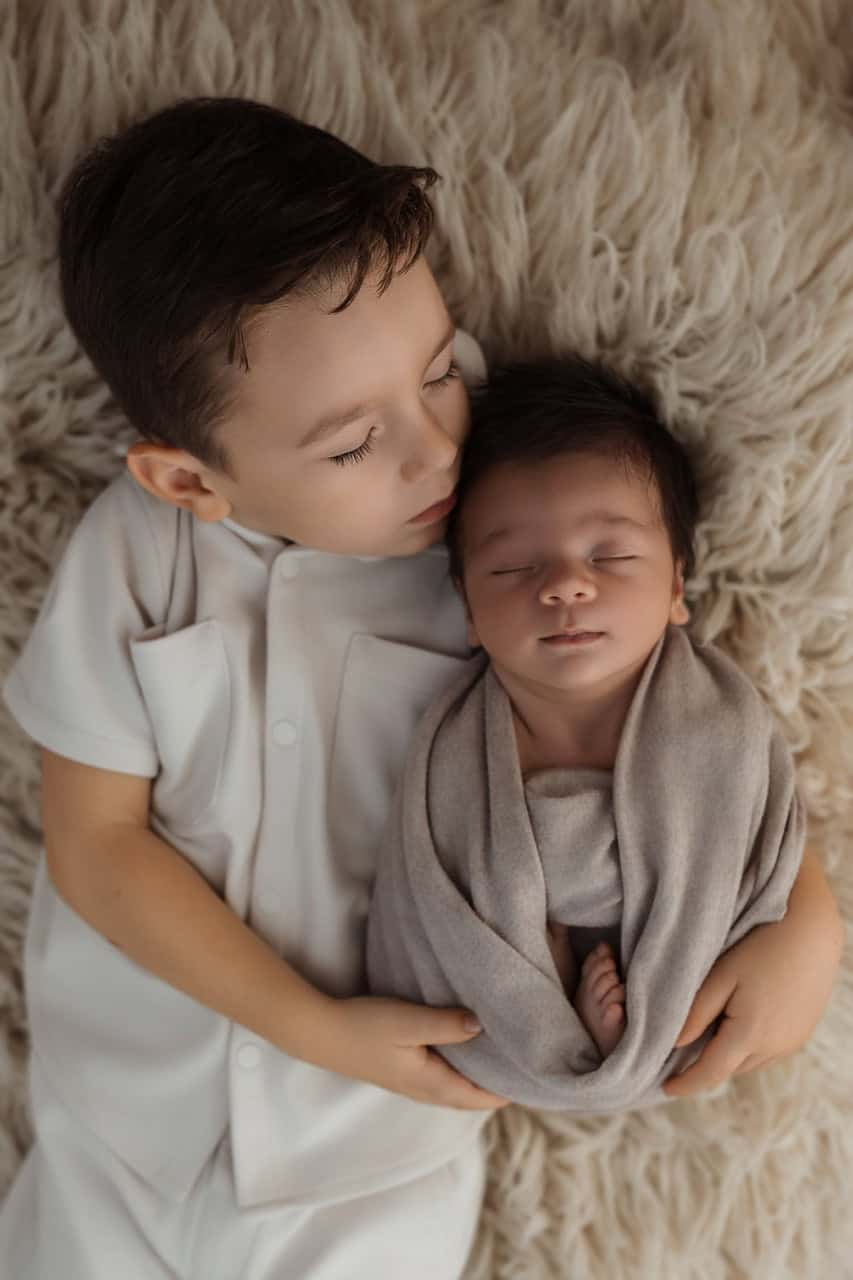Grand frère allongé avec son petit frère nouveau-né pendant une séance photo naissance